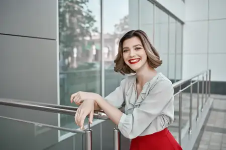 Женщина позирует с улыбкой на улице возле здания, передавая атмосферу повседневной жизни