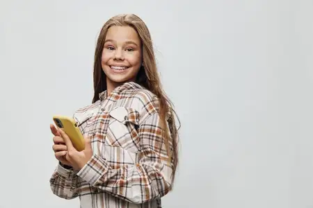 Улыбающаяся девушка в клетчатой рубашке держит жёлтый смартфон для переписки и использования социальных сетей