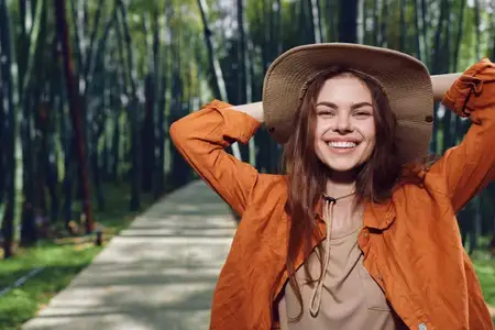 Женщина улыбается в шляпе, сфотографированная в парке на обсаженной деревьями тропе