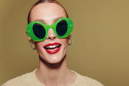 Счастливая женщина в больших зелёных солнцезащитных очках и с красной помадой уверенно улыбается