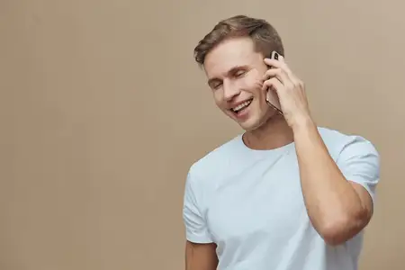 Улыбающийся мужчина наслаждается приятным разговором по мобильному телефону, одетый в повседневную голубую футболку, с радостным и расслабленным поведением