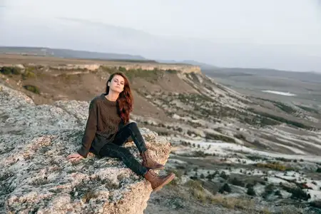 Спокойная женщина сидит на камне, любуясь величественным видом на горы во время золотого заката