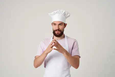 Веселый шеф-повар в белом фартуке жестикулирует руками в ресторанной кухне, обращаясь к профессионалам