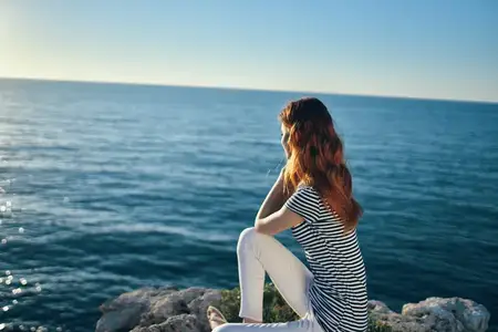 Женщина сидит на пляже у моря в горах и смотрит на закат
