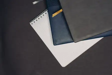 На сером фоне лежат блокноты, документы, книги и ручки