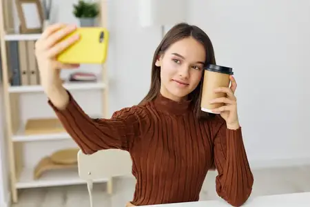 Девушка-студентка и фрилансер улыбается, делая селфи с ноутбуком и телефоном