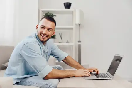Этот улыбающийся мужчина работает за ноутбуком в светлом и привлекательном современном рабочем пространстве