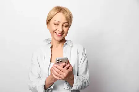 Улыбающаяся пожилая женщина держит смартфон в студийном портрете