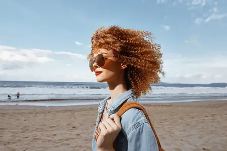 Улыбающаяся женщина с рюкзаком наслаждается свободой во время отпуска на пляже
