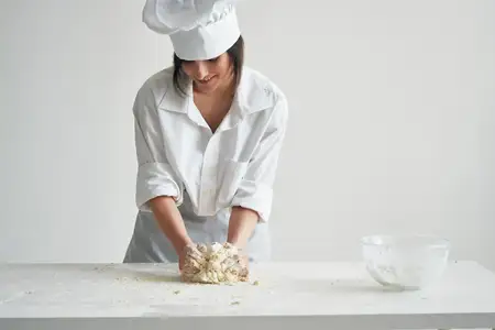 Женщина-пекарь в поварской форме работает с тестом и мучными изделиями