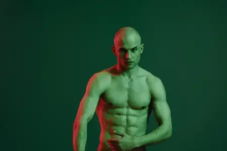 Это поразительное изображение представляет сильного мужчину, демонстрирующего свое скульптурное тело на фоне драматичного зеленого фона