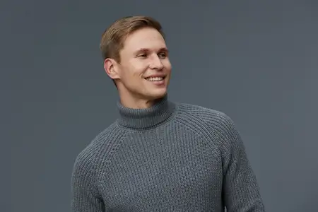 Улыбающийся мужчина в сером свитере смотрит в сторону со счастливым и расслабленным выражением лица
