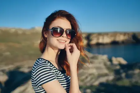 Красивая рыжеволосая женщина в футболке и солнцезащитных очках на природе в горах у реки