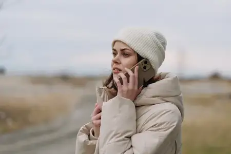 Уличная сцена: женщина в уютном зимнем наряде разговаривает по мобильному телефону