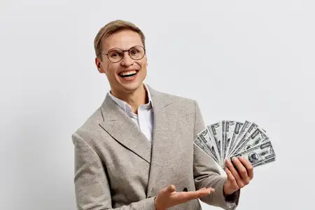 Счастливый профессиональный мужчина в очках демонстрирует наличные доллары, празднуя финансовое достижение