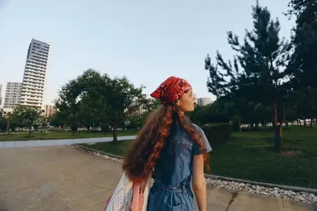Женщина, ведущая активный образ жизни, одетая в современный бохо-вестерн деним в стиле стрит-стайл с красной банданой и длинными волосами, идет на открытом воздухе в городском парке