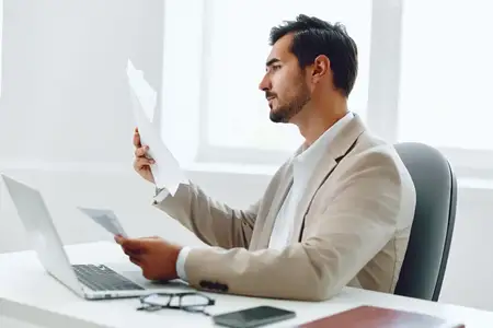 Руководитель в деловом костюме планирует работу с документами за ноутбуком в офисе