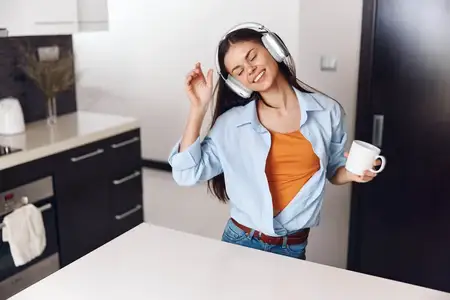 Женщина наслаждается утренним кофе и музыкой на кухне, надев наушники