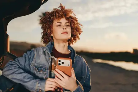 Женщина делает селфи на смартфон, джинсовая куртка, вьющиеся волосы, закат, дорога, путешествие, стиль жизни на открытом воздухе, портрет женщины, держащей мобильную камеру, интерьер машины…