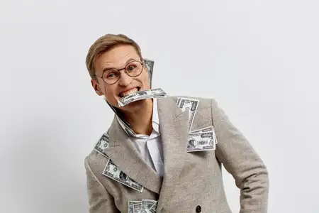 Улыбающийся мужчина с деньгами выглядит счастливым и взволнованным, кусает долларовые банкноты, в очках и клетчатом бежевом пиджаке, изолирован на белом фоне