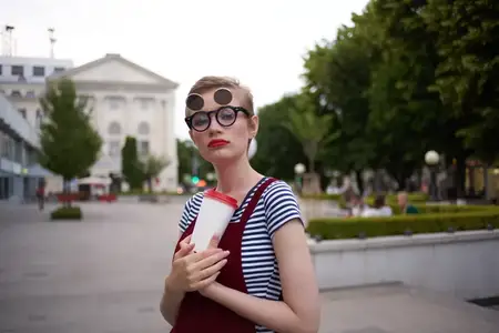 Женщина с короткой стрижкой и стаканом кофе прогуливается на свежем воздухе