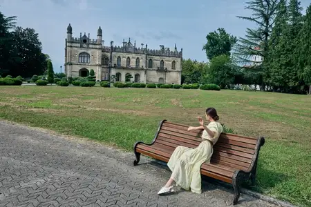 Женщина на скамейке у особняка в парке, аутентичность, инклюзивность, женщина сидит на скамейке в светлом платье