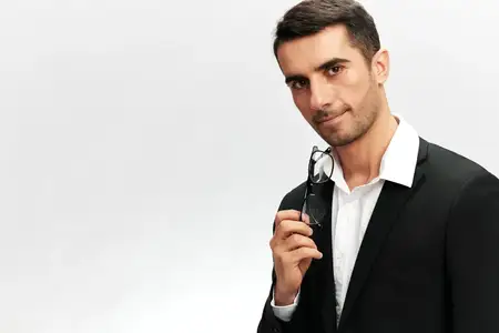 Менеджер по маркетингу, успешный бизнесмен в деловом костюме с очками в руках смотрит в камеру, излучая самоуверенность