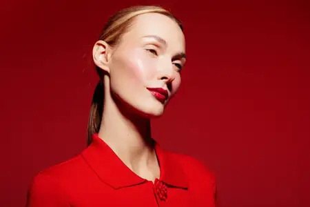 Стильная женщина с гладкими волосами и ярко-красными губами в красном наряде стоит перед красным фоном