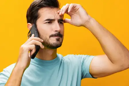 Мужчина в очках широко улыбается, показывая зубы, и держит смартфон, указывая на экран