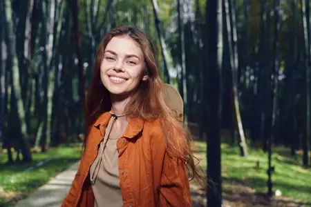 Портрет улыбающейся женщины на лесной тропе с рюкзаком и в пальто
