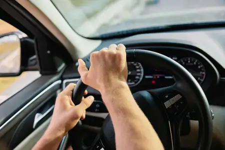 Руки сжимают руль автомобиля во время движения, подчёркивая сосредоточенность и контроль