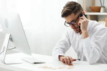 Привлекательный бизнесмен в белой рубашке сидит за компьютером с телефоном в офисе