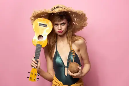 Женщина держит укулеле, кокосовый коктейль и пляжную шляпу