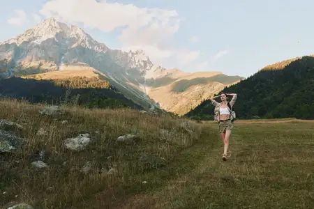 Женщина-туристка на залитом солнцем лугу с далёкими горами, рюкзак готов к путешествию