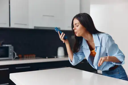 Женщина пользуется смартфоном на кухне, стоя на столешнице