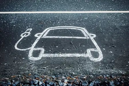 Контур электромобиля, нарисованный мелом на темной асфальтовой поверхности, с зарядной вилкой, пропагандирующий устойчивое развитие и чистую энергию
