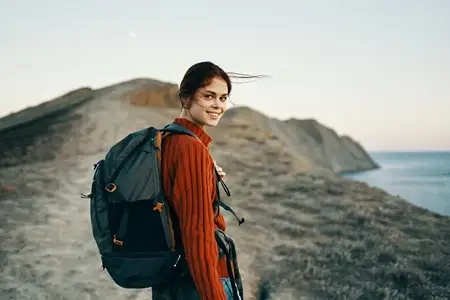 Счастливая женщина с рюкзаком идет по тропе в горах у моря, наслаждаясь свежим воздухом на природе