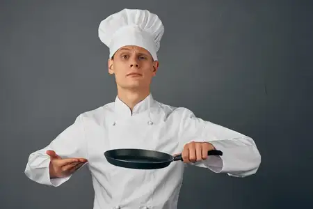 В кафе повар в униформе держит сковороду в руках, занимаясь приготовлением пищи в ресторане