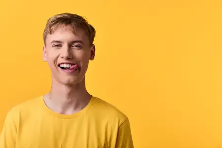 Молодое выражение лица, игривое настроение, яркий цвет, желтый фон, повседневная мода, счастливая улыбка, жизнерадостная атмосфера, студийный снимок, запечатлевший беззаботный момент с ярким цветом…