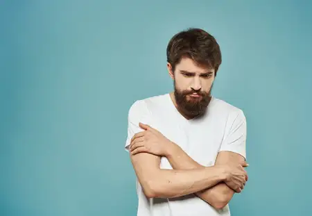 Мужчина в белой футболке на синем фоне жестикулирует руками, у него печальный взгляд