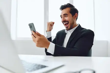 Мужчина-бизнесмен в современном костюме сидит за столом в офисе, работает за ноутбуком и одновременно разговаривает по телефону