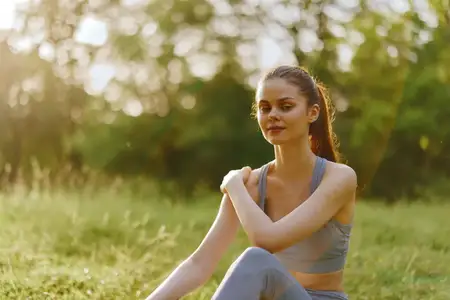 Молодая женщина в спортивной одежде мирно сидит в зелёном парке, олицетворяя здоровье и физическую форму