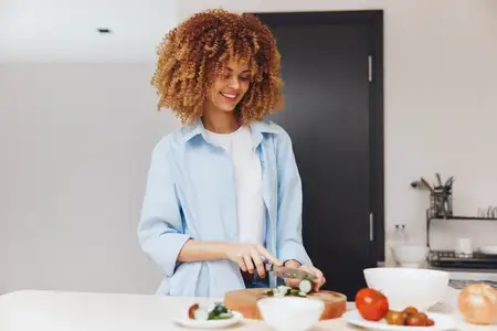 Счастливая афроамериканка готовит вкусную еду на своей домашней кухне, улыбается и наслаждается домашними делами и кулинарными хобби
