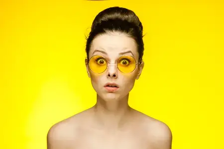 Брюнетка с обнажёнными плечами, жёлтые очки, эмоции, кадр крупным планом, студия