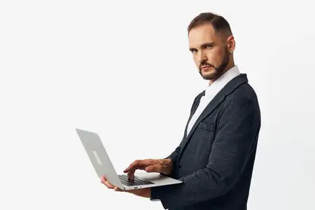 Изображение запечатлевает уравновешенного мужчину-профессионала, демонстрирующего концентрацию и амбиции, работающего за элегантным ноутбуком в чистой студийной обстановке