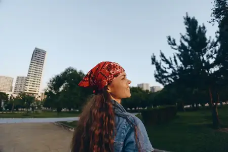 Женщина, ведущая активный образ жизни, одетая в современную джинсовую уличную одежду в стиле бохо-вестерн, уверенно улыбается, наслаждаясь отдыхом в городском парке с деревьями и зданиями