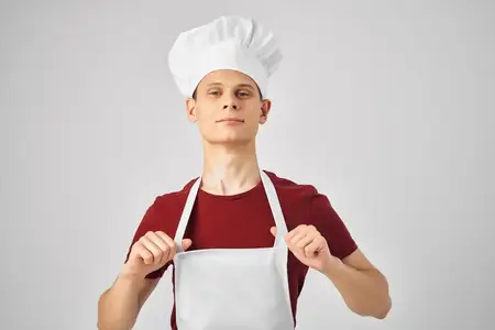Мужчина в белом фартуке и колпаке на голове, рабочая униформа, на кухне