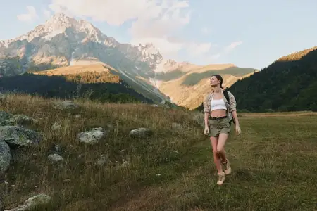 Активная женщина совершает поход в горах в повседневной летней одежде и с рюкзаком