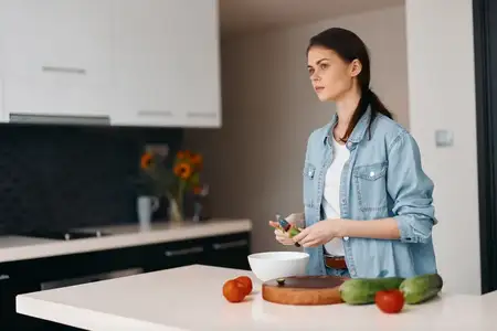 Здоровая молодая женщина-шеф-повар стоит на кухне и готовит свежий вегетарианский салат на столе