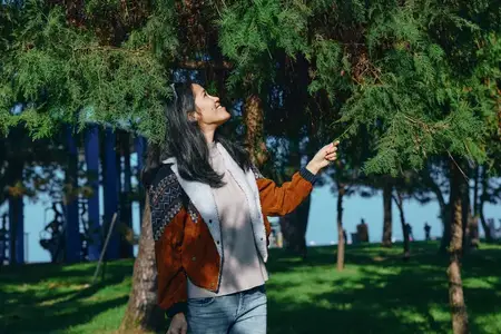Природа, женщина, сцена в городском парке с деревьями, солнечным светом и уютной курткой, когда она наслаждается ветерком, исследованием, отдыхом и безмятежностью среди зелени и открытого неба